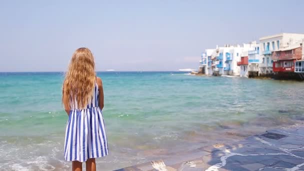 Adorable niña en Little Venice la zona turística más popular de la isla de Mykonos, Grecia. Hermosa sonrisa de niño y mirar a la cámara en el fondo de Little Venice . — Vídeo de stock