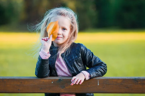 Amazing little girl outdoors at beautiful warm day in autumn park with yellow leaf in fall — Stock Photo, Image