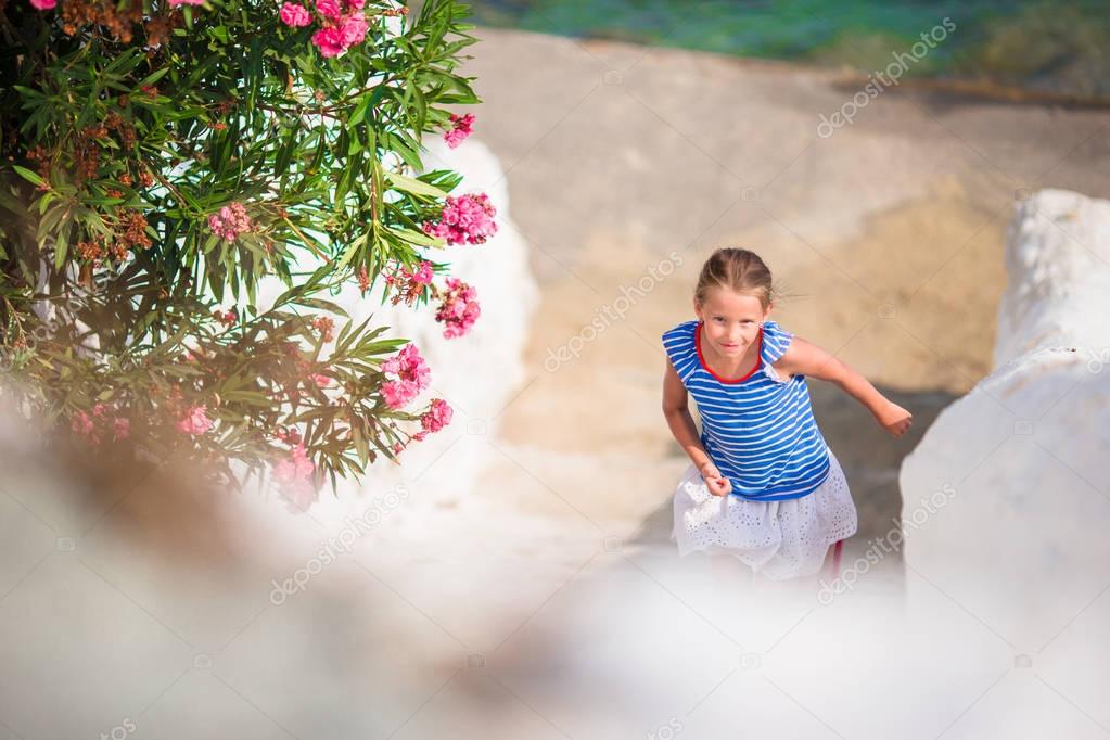 Adorable girl having fun outdoors. Kid at street of typical greek traditional village with white walls and colorful doors on Mykonos Island, in Greece