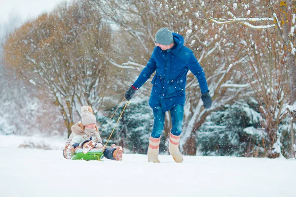 Niñas disfrutando del trineo en el día de invierno. Padre tirando en trineo a sus adorables hijas. Vacaciones familiares en Nochebuena al aire libre — Foto de Stock