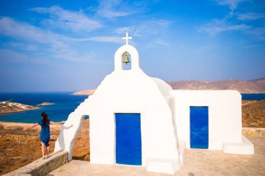 Yunanistan 'ın Mykonos adasında deniz manzaralı genç kadın ve geleneksel beyaz kilise