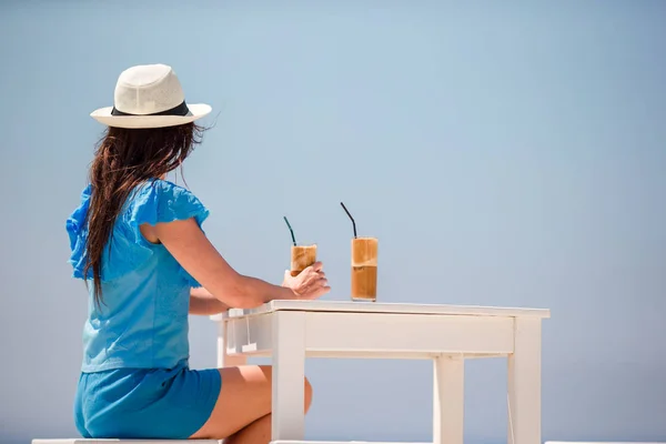 Молода дівчина п'є холодну каву, насолоджуючись видом на море. Красива жінка відпочиває під час екзотичних відпусток на пляжі насолоджуючись тріумфом — стокове фото