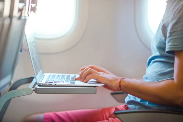 Junger Mann sitzt im Flugzeug und arbeitet an seinem Laptop — Stockfoto