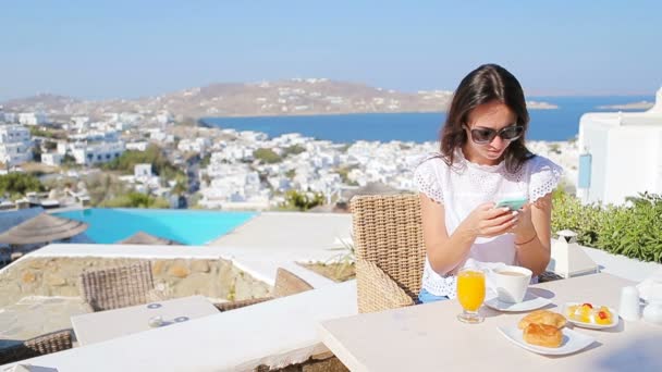 Piękna dama elegancki na śniadanie z telefonu w kawiarni na świeżym powietrzu z niesamowitym widokiem na miasto Mykonos. — Wideo stockowe