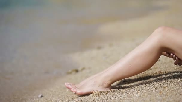 Female slender smooth legs on white sand beach — Stock Video