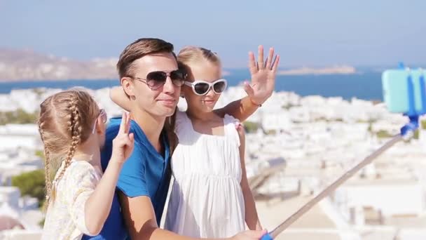 Vacaciones familiares en Europa. Padre e hijos tomando selfie antecedentes Mykonos ciudad en Grecia — Vídeo de stock