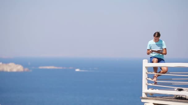 Caucásico chico relajante cerca de la piscina con una vista increíble y libro de lectura en Grecia. Hermoso fondo famoso — Vídeos de Stock