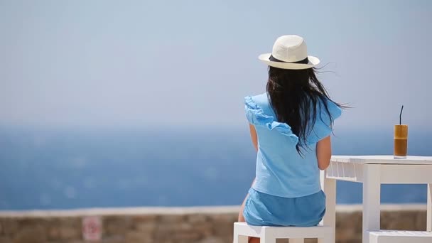 Νεαρό κορίτσι πόσιμο κρύο καφέ απολαμβάνοντας τη θέα στη θάλασσα. Όμορφη γυναίκα να χαλαρώσετε κατά τη διάρκεια της εξωτικό διακοπές στην παραλία απολαμβάνοντας φραπέ — Αρχείο Βίντεο