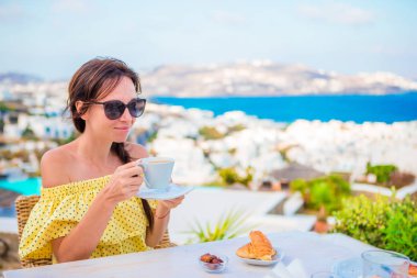 Mikonos kentine muhteşem manzaralı açık kafede kahvaltı güzel kız. Resort Restoran deniz manzaralı lüks otel terasında sıcak kahve içme kadın.
