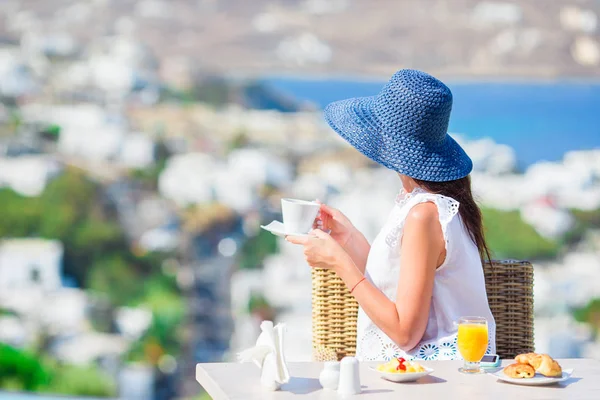 Bella ragazza elegante che fa colazione al caffè all'aperto con splendida vista sulla città di Mykonos. Donna che beve caffè caldo sulla terrazza dell'hotel di lusso con vista mare al ristorante del resort . — Foto Stock