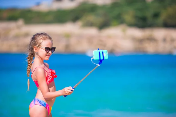 Mała dziewczynka biorąc autoportret przez jej smartphone na plaży. Dziecko, ciesząc się jej urlop suumer i robienia zdjęć do pamięci — Zdjęcie stockowe