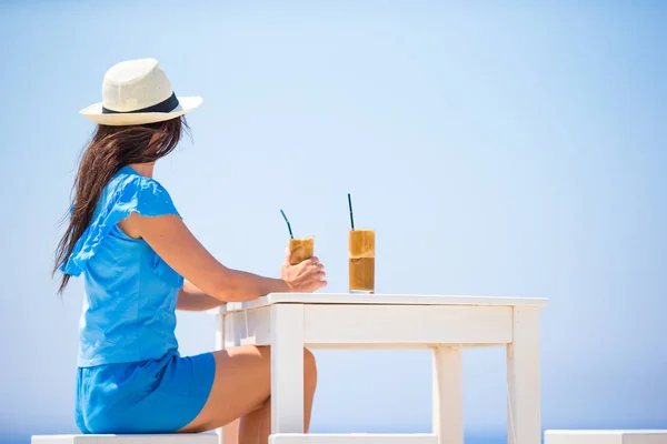 Mujer joven bebiendo café frío disfrutando de vistas al mar. Hermosa mujer relajarse durante vacaciones exóticas en la playa disfrutando de frappe — Foto de Stock