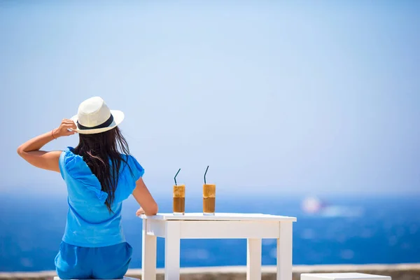 Młoda kobieta pije zimną kawę podziwiając widok na morze. Piękna kobieta zrelaksować się podczas egzotycznych wakacji na plaży korzystających frappe — Zdjęcie stockowe