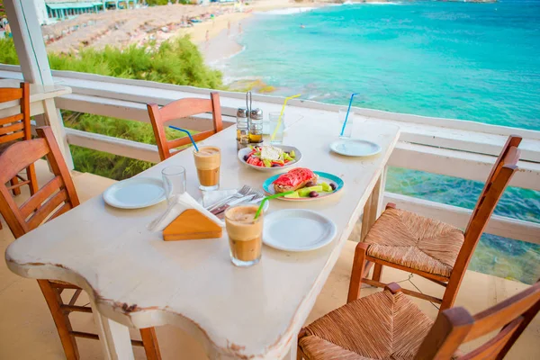 伝統的なランチとおいしい新鮮なギリシャ サラダやフラッペ、昼食のための屋外レストランで、海と港の美しい景色添え brusketa — ストック写真