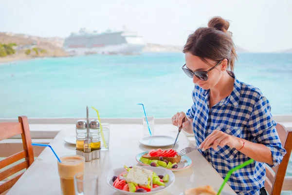 Νεαρή γυναίκα το γεύμα με νόστιμη σαλάτα, φραπέ και brusketa σερβίρονται για μεσημεριανό γεύμα στο υπαίθριο εστιατόριο με όμορφη θέα στη θάλασσα και λιμάνι — Φωτογραφία Αρχείου