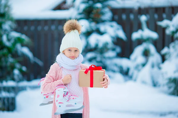 可爱的小女孩，在圣诞节那天拿着礼物和溜冰鞋户外穿保暖的衣服 — 图库照片