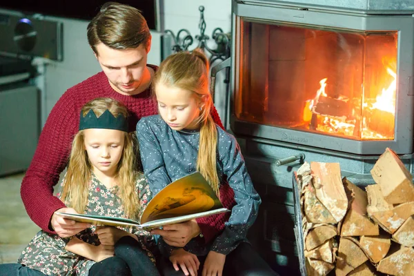 Apa és a két kis gyerekek könyvet olvas, és pihentető a kandalló mellett néhány hideg onchristmas Szilveszter este — Stock Fotó