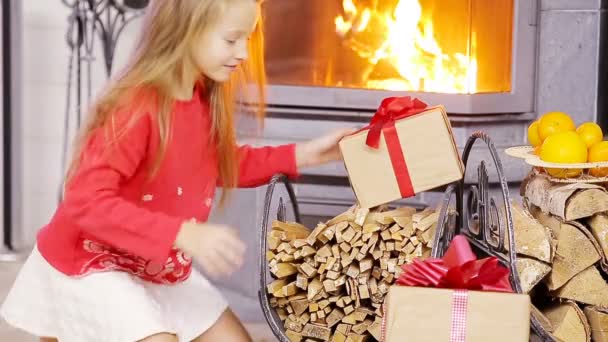 Smiling nice girl opening christmas present near fireplace — Stock Video