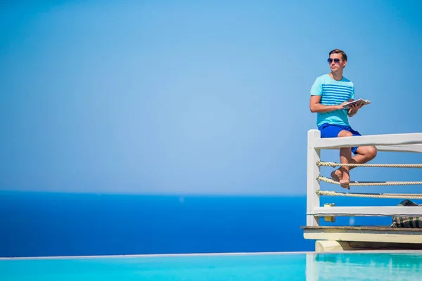 Ragazzo caucasico rilassante vicino alla piscina con vista mozzafiato e libro di lettura in Grecia. Bellissimo sfondo famoso — Foto Stock
