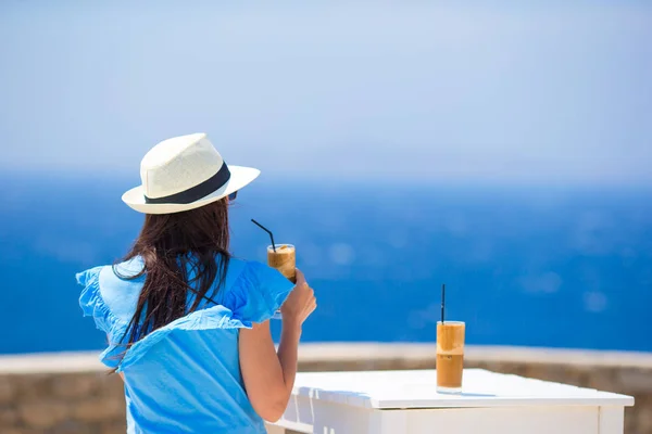 Visão traseira da mulher bebendo café frio apreciando vista para o mar. Mulher bonita relaxar durante as férias marítimas europeias na praia desfrutando frappe — Fotografia de Stock