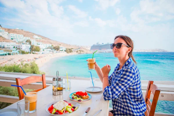 Ung kvinna lunch med läckra färska grekiska sallad, frappe och brusketa som serveras till lunch på uteservering med vacker utsikt över havet och hamnen — Stockfoto