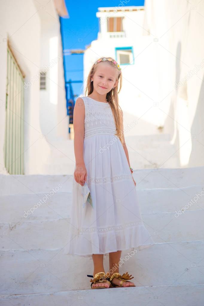 Adorable girl outdoors in greek village. Kid at street of typical greek traditional village with white stairs on greek island