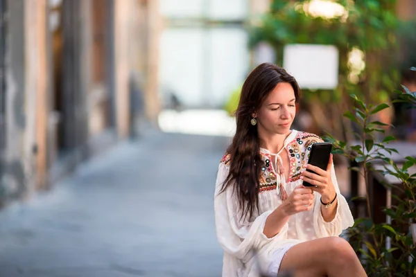 Retrato de una hermosa mujer sentada en una cafetería al aire libre bebiendo café y usando un teléfono inteligente. Chica joven mirando en la pantalla . — Foto de Stock