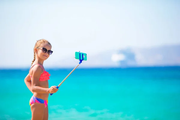 Menina tomando auto-retrato por seu smartphone na praia. Kid aproveitando suas férias suumer e fazer fotos de fundo do mar — Fotografia de Stock