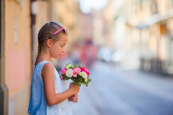 Adorable little girl with flowers bouquet walking in european city — Stock Photo, Image