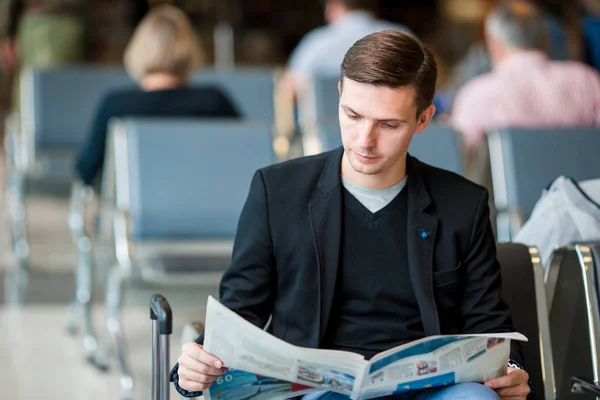 Young man reading newspaper at the airport while waiting for boarding. Casual young businessman wearing suit jacket. — Stock Photo, Image