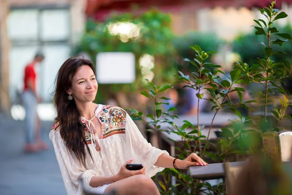 美丽的女人坐在户外咖啡馆喝咖啡，使用智能手机的肖像 — 图库照片