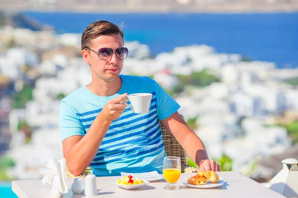 Giovane ragazzo con caffè caldo in caffè all'aperto con splendida vista sulla città di Mykonos . — Foto Stock