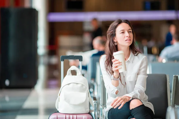 Ung kvinna med kaffe i en flygplatslounge väntar flyg flygplan. — Stockfoto