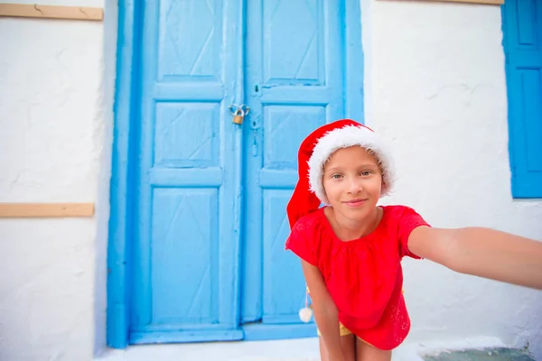 Urocza dziewczynka w Santa Hat biorąc selfie na wąskiej uliczce w greckiej wioski — Zdjęcie stockowe