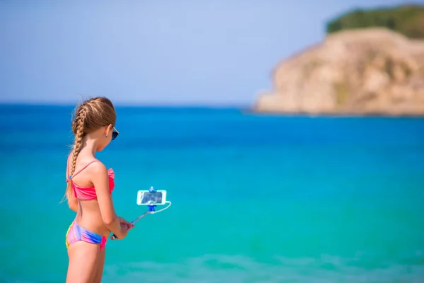 Маленькая девочка делает автопортрет по мобильному телефону на пляже. Ребенок наслаждается ее suumer отпуск и делает фотографии фоне моря — стоковое фото