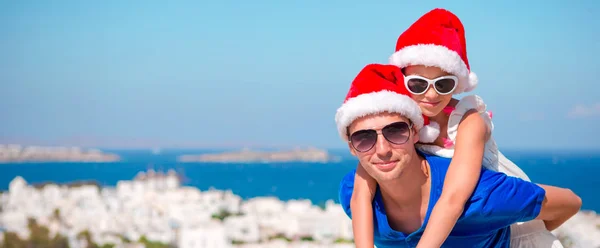 Portret małej dziewczynki i szczęśliwy tata w Santa kapelusze cieszyć się wakacje świąteczne z pięknym widokiem. Panorama na stare miejscowości Mykonos w Grecji. — Zdjęcie stockowe