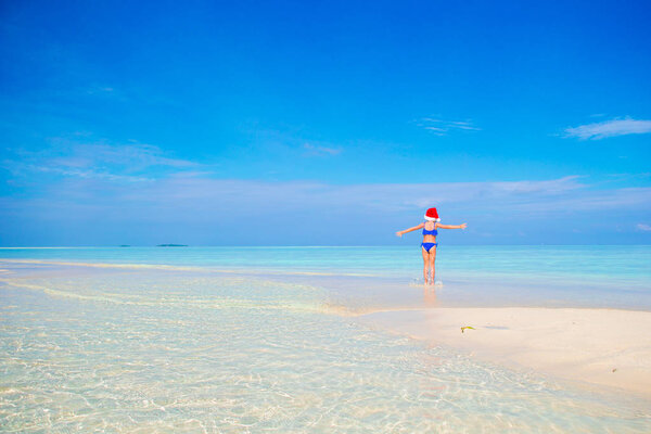 Little girl in Santa hat on white beach during Xmas vacation