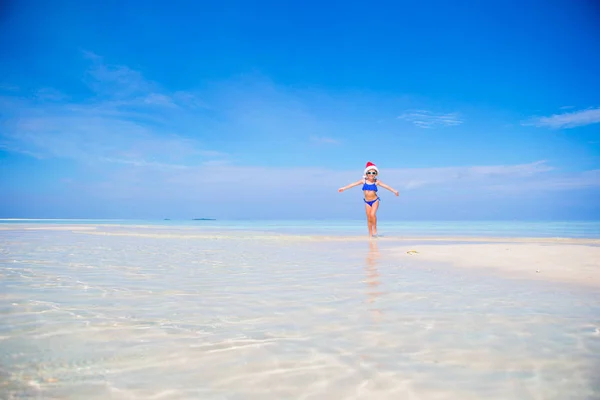 Niña en sombrero de Navidad en la playa blanca durante las vacaciones de Navidad —  Fotos de Stock