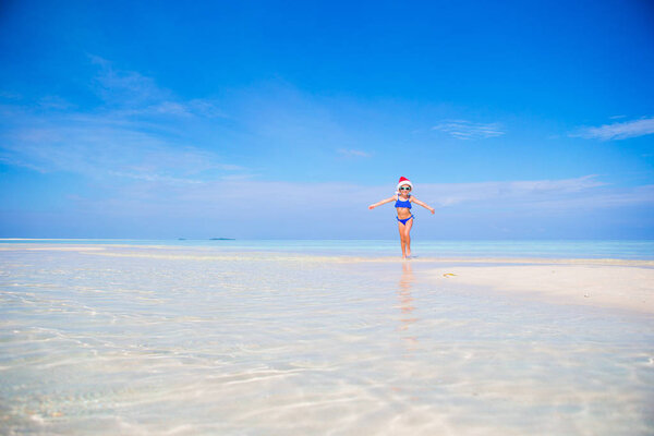 Little girl in Christmas hat on white beach during Xmas vacation
