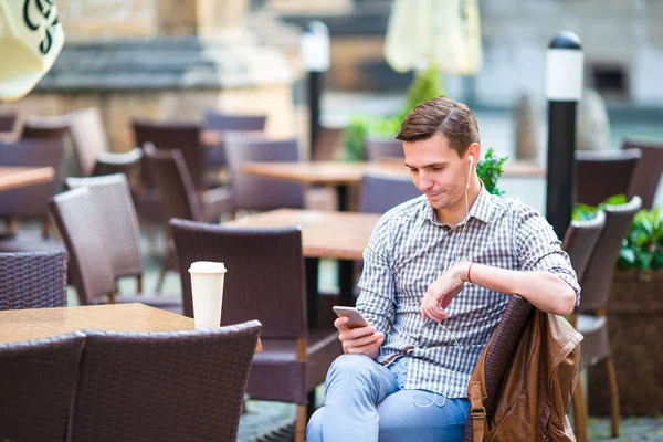 Jovem com celular ao ar livre no café ao ar livre. Homem usando smartphone móvel . — Fotografia de Stock