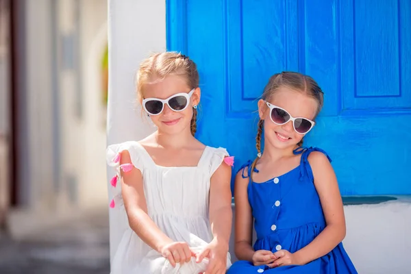 Portret van weinig lachende meisjes zitten in de buurt van oude blauwe deur in Griekse Mykonos dorp, Grieks — Stockfoto