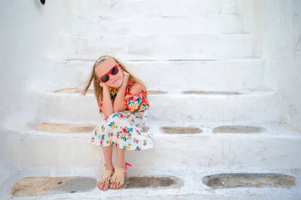 Liten söt tjej porträtt utomhus i gammal grekisk by. Kid på gatan av typisk grekisk traditionell by med vita väggar och färgglada dörrar på Mykonos, Greklands ö — Stockfoto