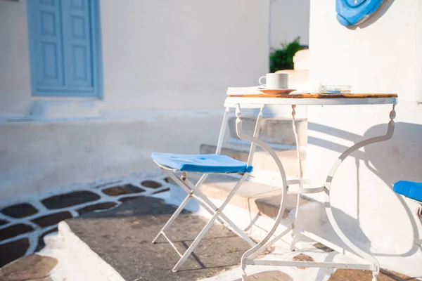 Beautiful cafe on a street of typical greek traditional village on Mykonos Island, Greece. Coffee on table for breakfast — Stock Photo, Image