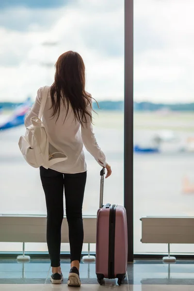 Mujer joven cerca de una gran ventana panorámica en un salón del aeropuerto a la espera de llegar —  Fotos de Stock