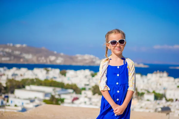 야외에서 파란 드레스에 작은 소녀. 흰 벽과 다채로운 문 미코노스 섬, 그리스에 전형적인 그리스 전통 마을의 거리에서 아이 — 스톡 사진