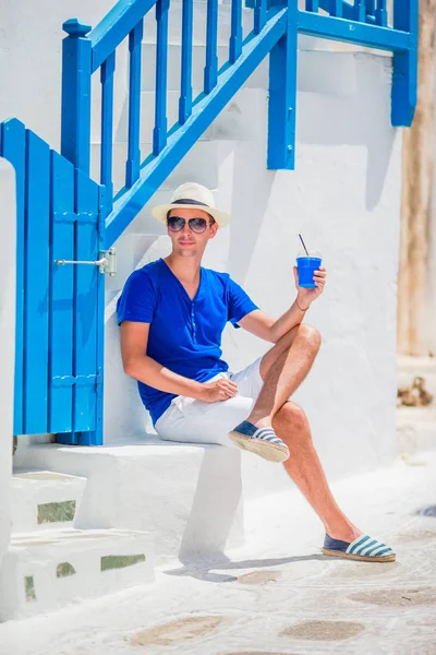 Man drinking coffee to go in traditional greek village outdoors. Young boy with hot coffee in outdoor cafe in Mykonos town. — Stock Photo, Image