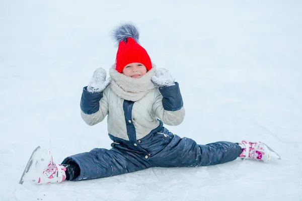 Kleines entzückendes Mädchen sitzt nach Sturz mit Schlittschuhen auf dem Eis — Stockfoto