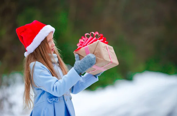 Очаровательная маленькая девочка с рождественским подарком зимой на свежем воздухе — стоковое фото