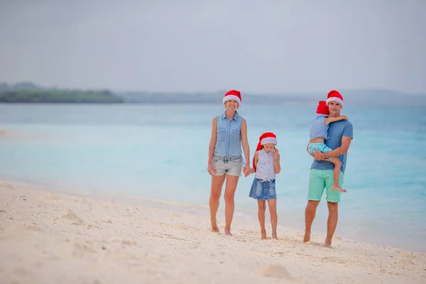 Happy family in red Santa hats on tropical beach celebrating Christmas — Stock Photo, Image