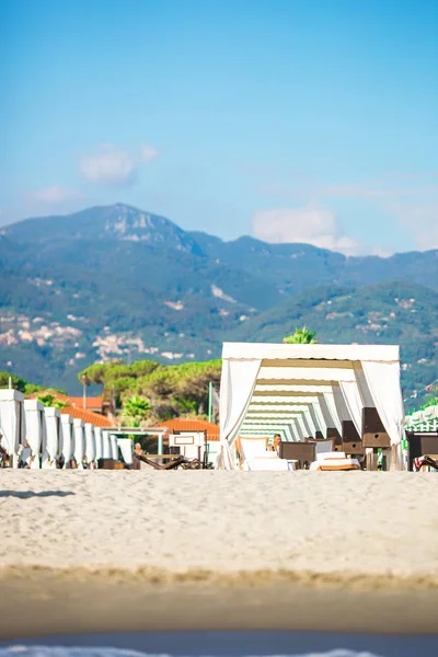 Camas de sol de madeira em frente a um mar azul-turquesa na luz da noite. Camas de sol na famosa praia de areia italiana no Forte dei Marmi — Fotografia de Stock